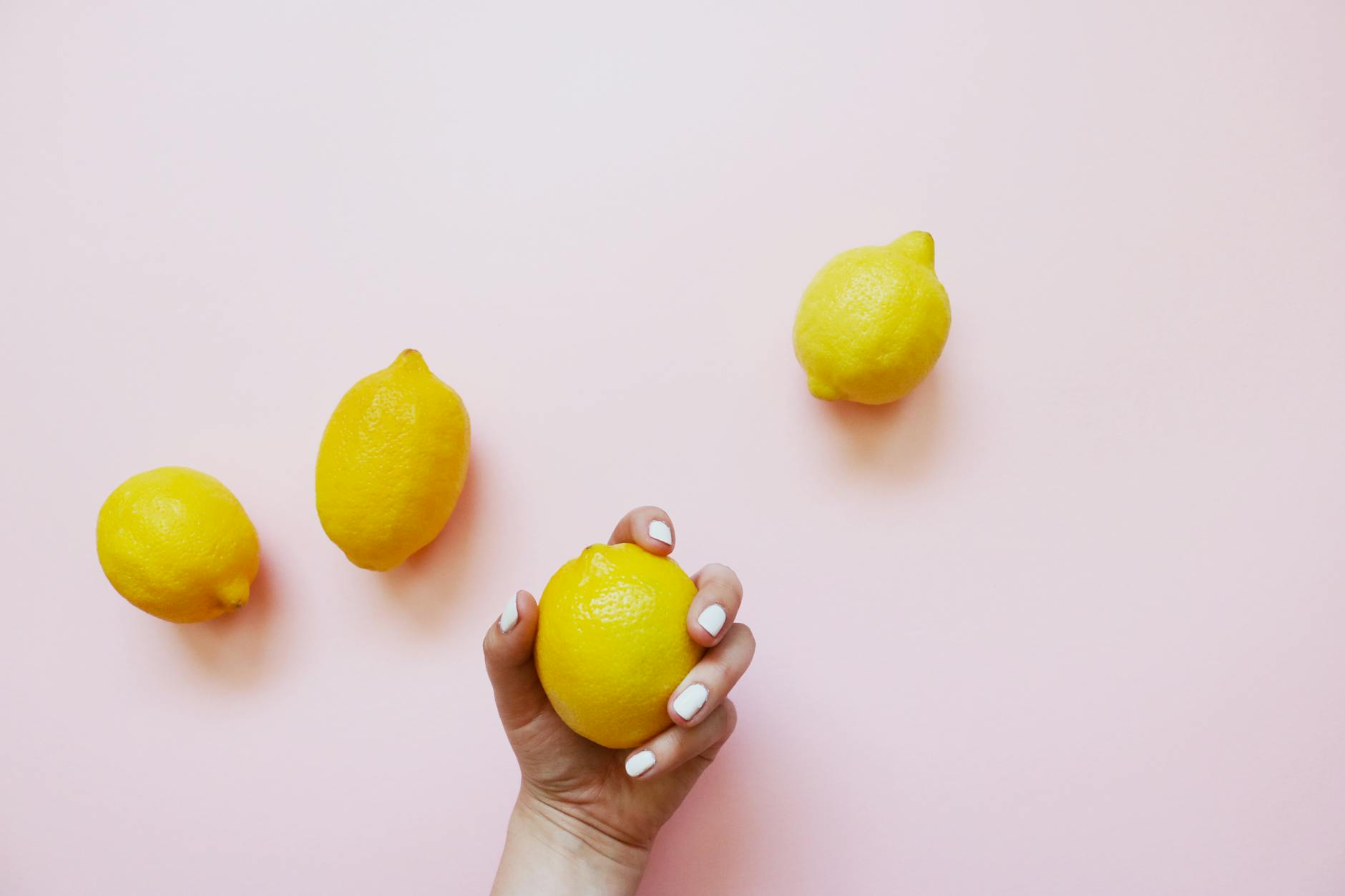 A hand holding a fresh lemon on a soft pink background, symbolizing reclaiming pleasure on your own terms