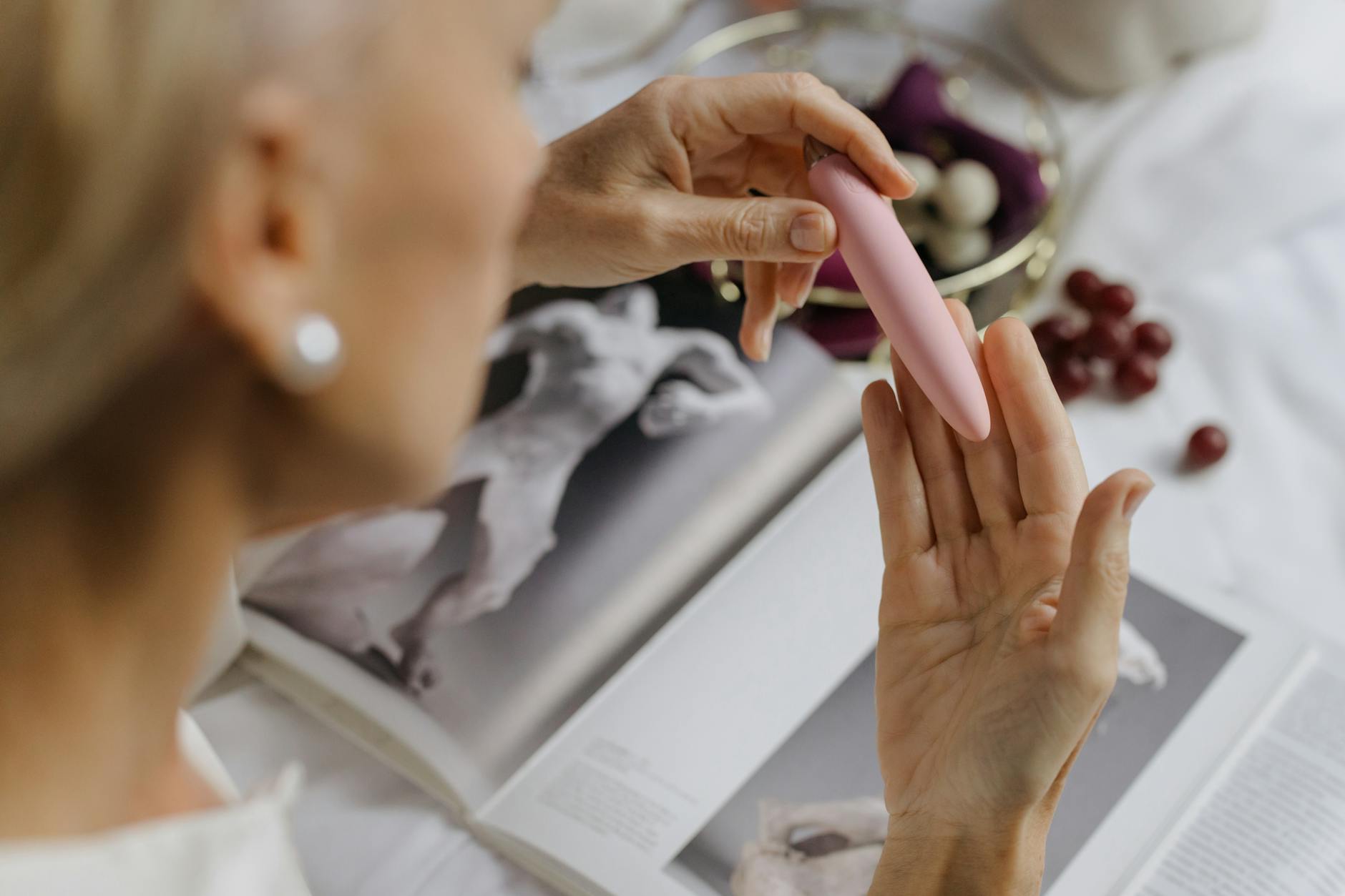 Hand holding a pink lemon vibrator with books in background, intimate and personal setting