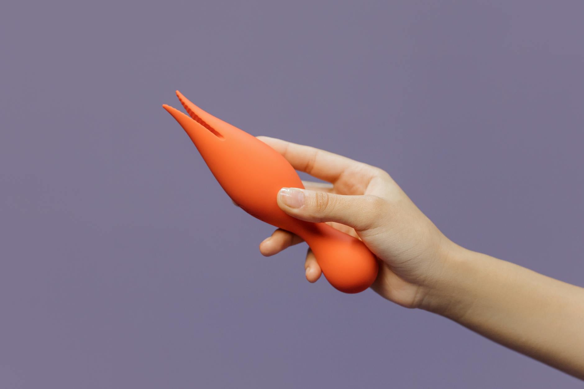 A hand holding a lemon-shaped vibrator against a minimalistic purple backdrop, showcasing modern sensuality and gentle touch