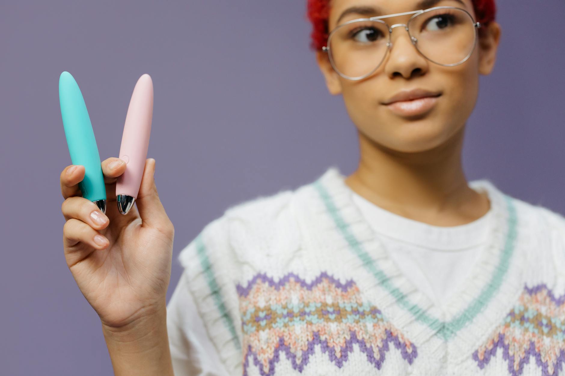 A close-up of hands holding a sleek blue vibrator against a purple background